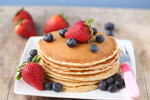 Close up of cottage cheese protein pancakes stacked on a plate with strawberries and blueberries