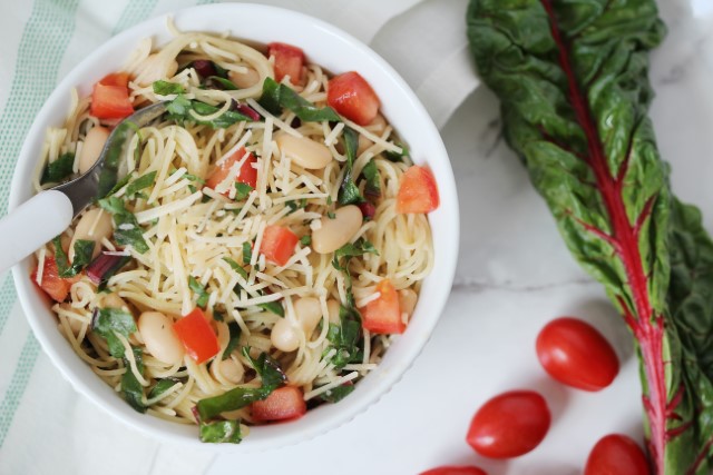 Garlic Pasta with Swiss Chard leaf next to bowl of pasta and 2 tomatoes